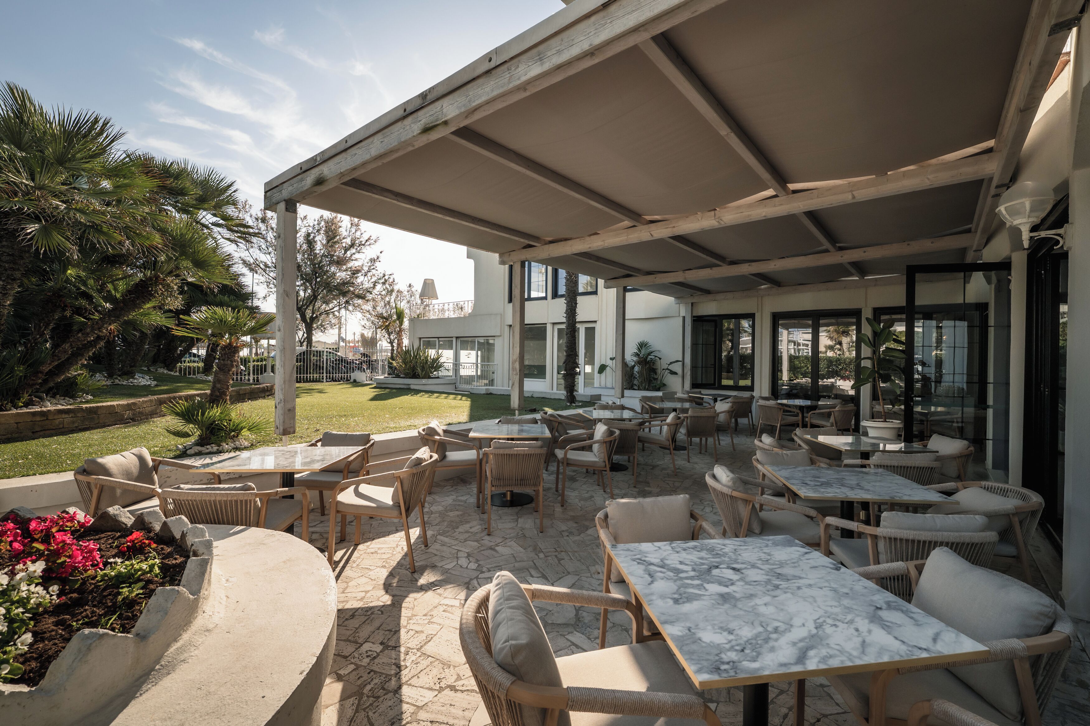 Un patio al aire libre con mobiliario de mimbre, mesas de mármol y vistas a un edificio moderno.