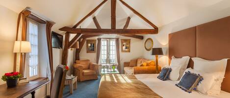 Une chambre d’hôtel avec un grand lit, un bureau avec une lampe, une chaise et une petite table sur laquelle est posée une plante.