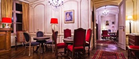 A formal dining room with a chandelier, red upholstered chairs, a wooden table, and a patterned rug.