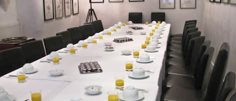 A conference room with a long table set for a meeting, equipped with chairs, a projector, and framed pictures on the walls.