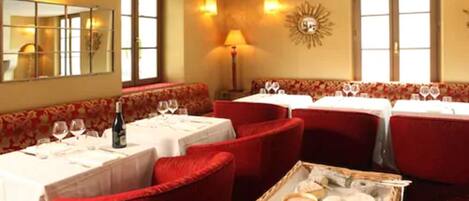 A restaurant with red upholstered booths, white tablecloths, and a tray of cheese and other items on the table.