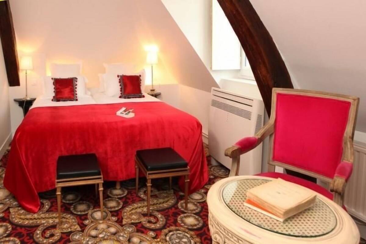 A room with a bed, two nightstands, a chair, a small table, and a decorative rug.