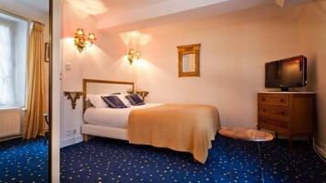 A hotel room with a bed, a television, a dresser, and a small stool.