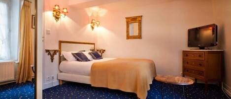 Une chambre d’hôtel avec un lit, une télévision, une commode et un petit tabouret.
