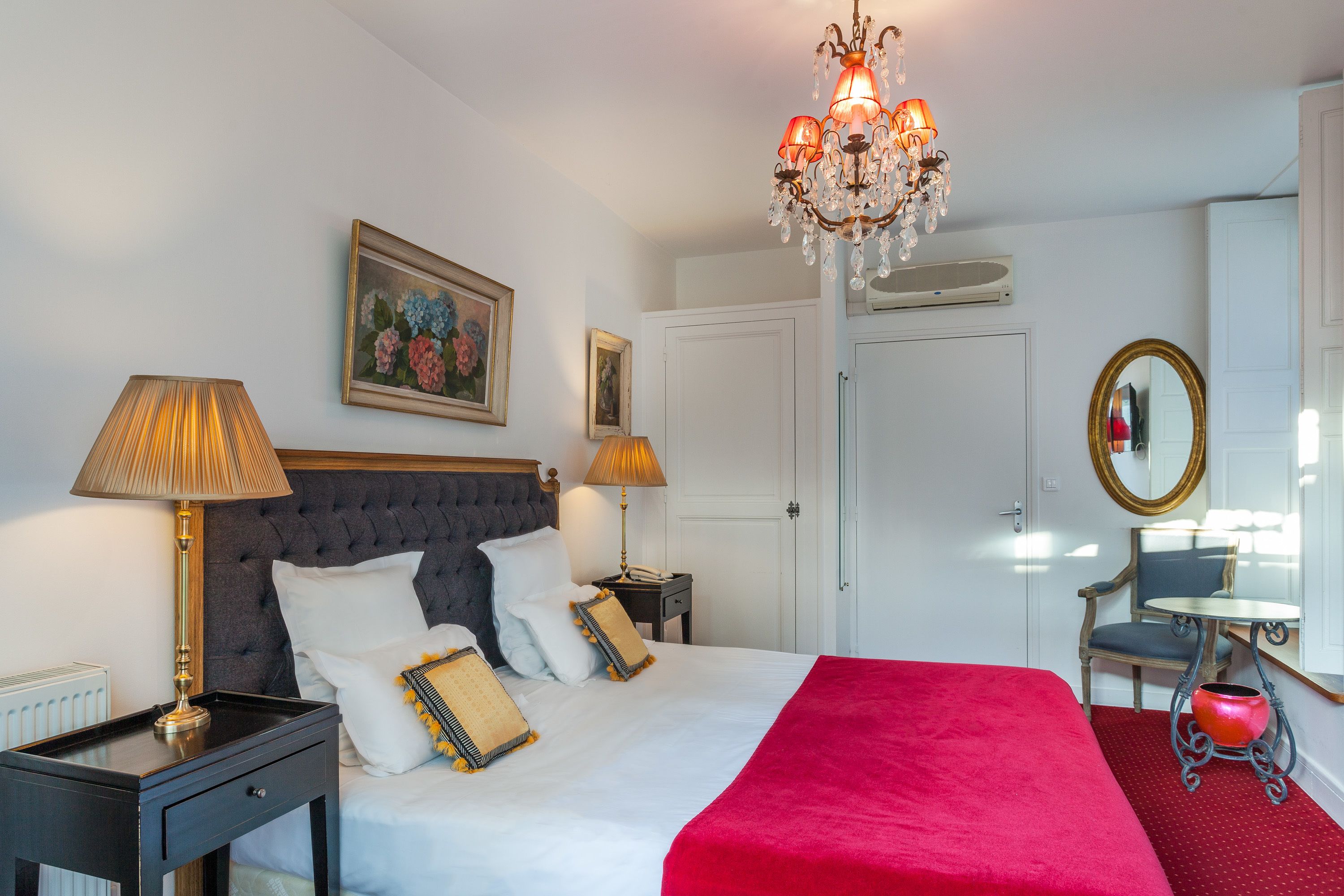 Quarto de hotel bem arrumado com uma cama grande, duas mesas de cabeceira, um lustre, um espelho e uma pequena mesa com uma cadeira.