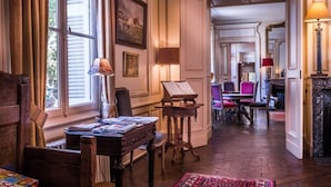 Una habitación con un piano, una mesa con revistas, una chimenea y vistas a otra estancia a través de un arco.