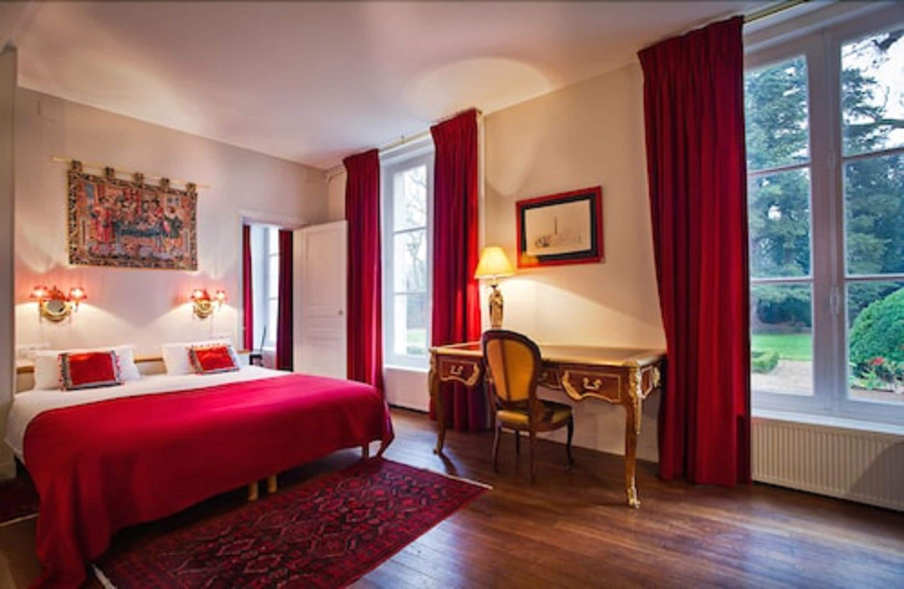 Ett hotellrum med en stor säng, ett skrivbord och en stol. Det finns ett fönster med gardiner, en tavla på väggen och en lampa på skrivbordet.