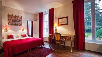 Habitación de hotel con una cama grande, un escritorio y una silla. Hay una ventana con cortinas, un cuadro en la pared y una lámpara sobre el escritorio.