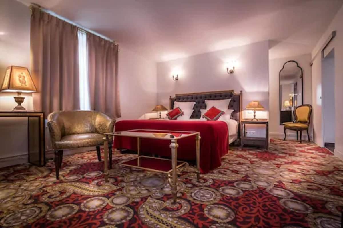 A hotel room with a large bed, a chair, a small table, and a carpeted floor.