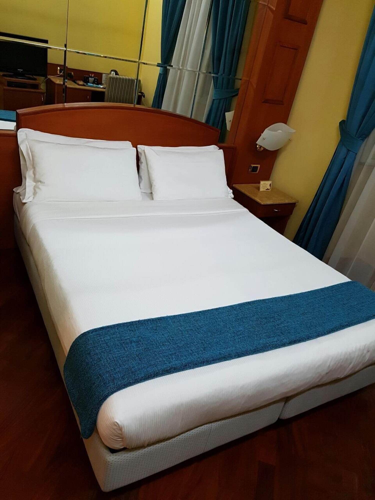 A hotel room with a bed, a nightstand, a lamp, and a television.