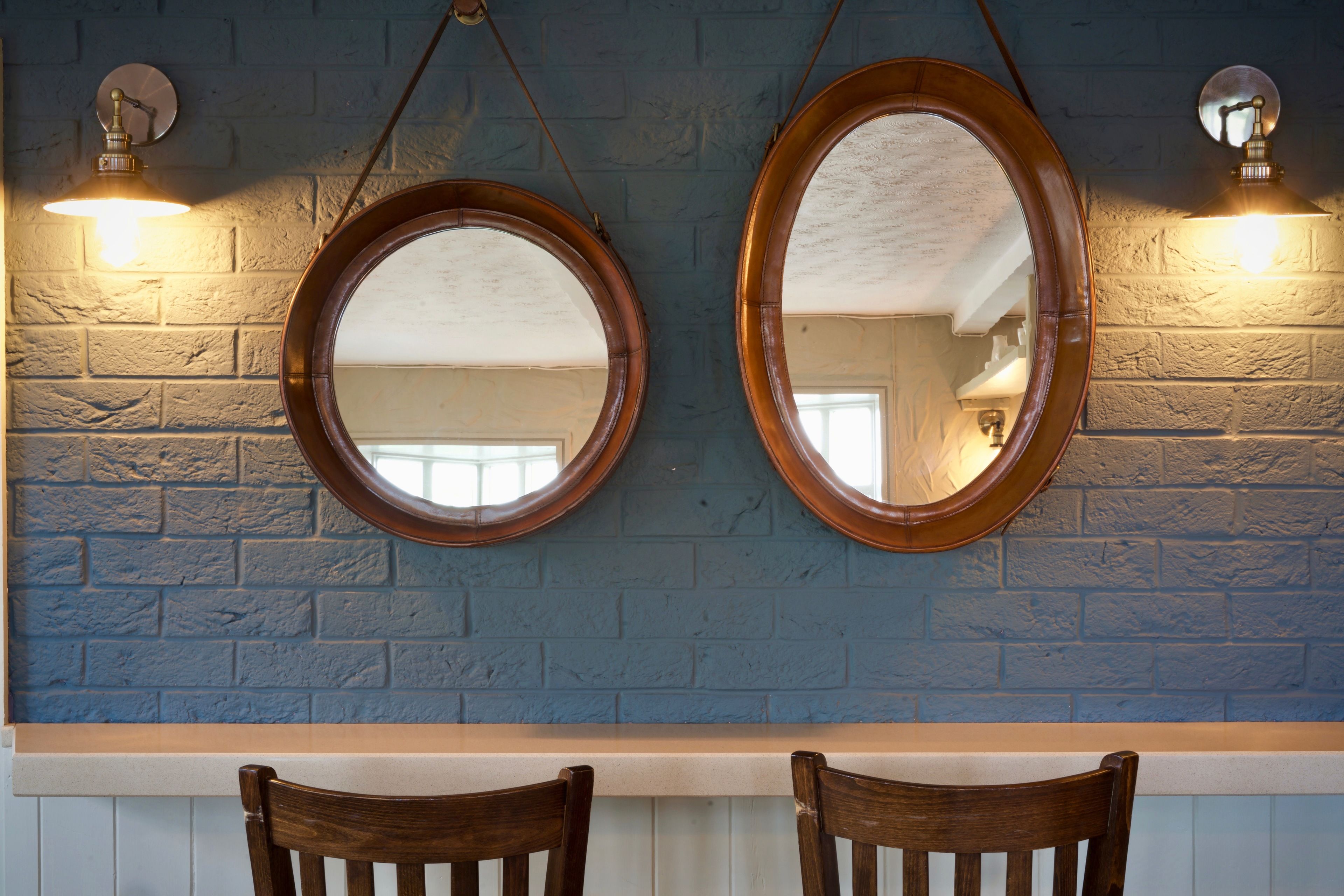 Two wooden-framed mirrors on a blue brick wall, with a white countertop below.
