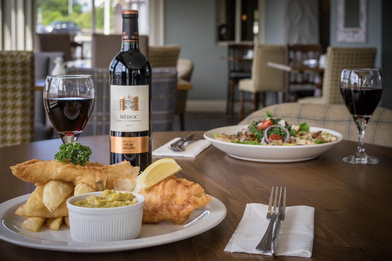 Un tavolo da pranzo con un piatto di fish and chips, una bottiglia di vino e un'insalata.