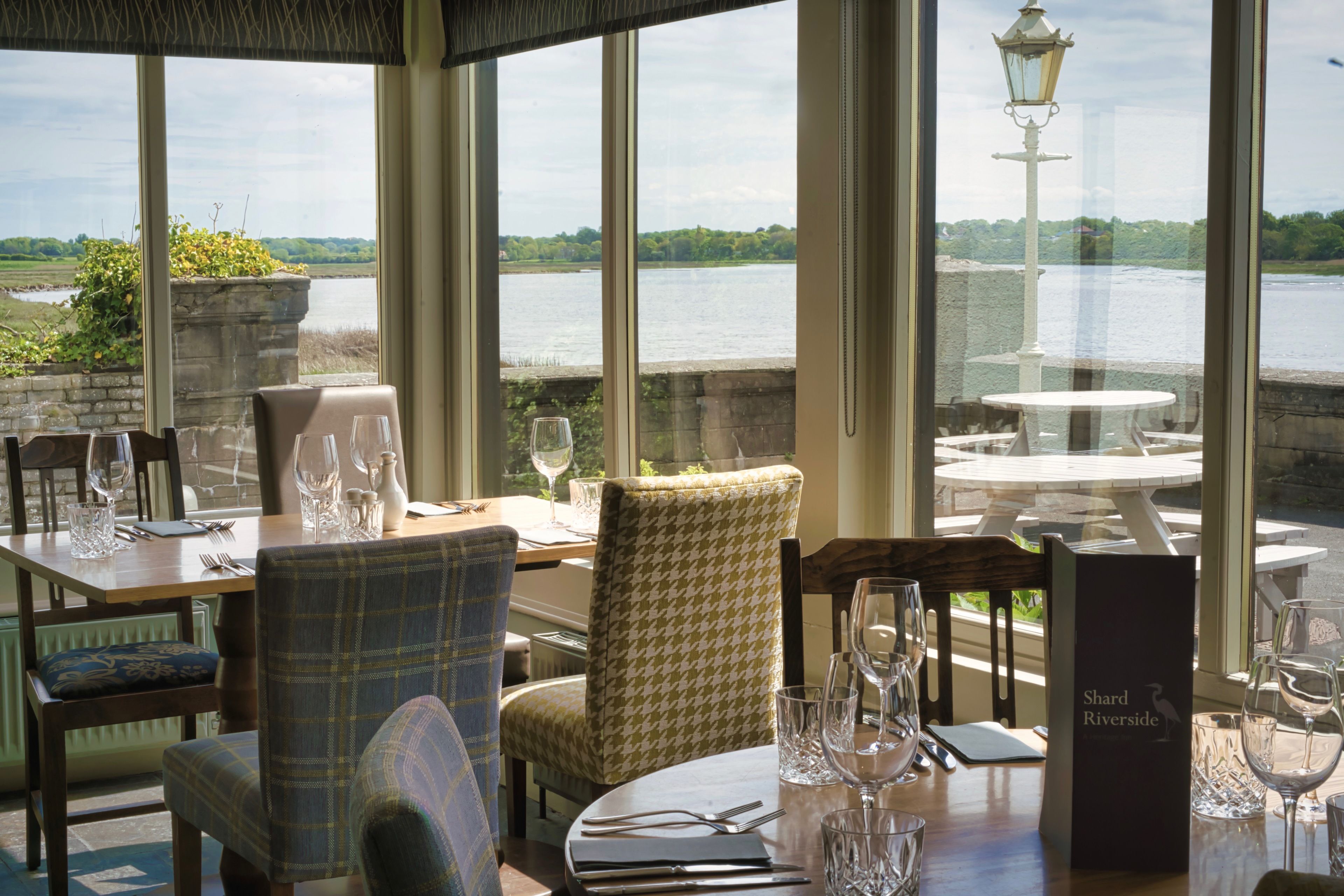 A dining area with tables set for two, chairs, and a view of a river.