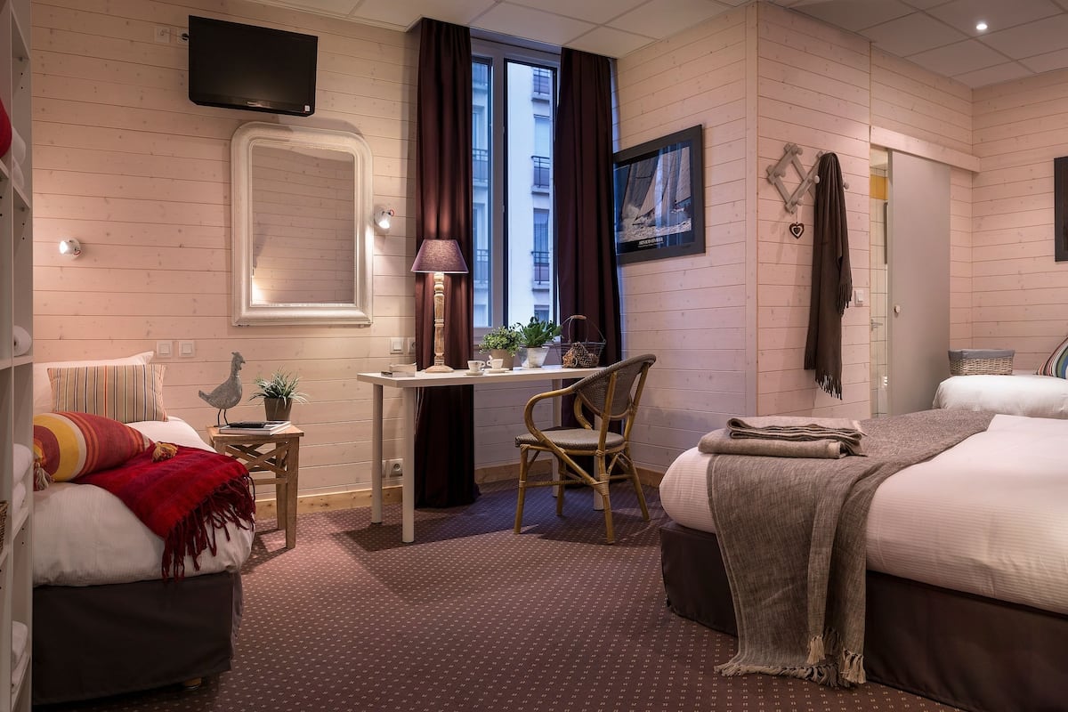 Ett mysigt hotellrum med en säng, ett skrivbord, en stol, en tv och ett fönster med gardiner.