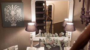 A well-lit room with a large mirror, two lamps, a decorative bird, and a framed picture on the wall. - Hôtel des Alpes (Annecy)