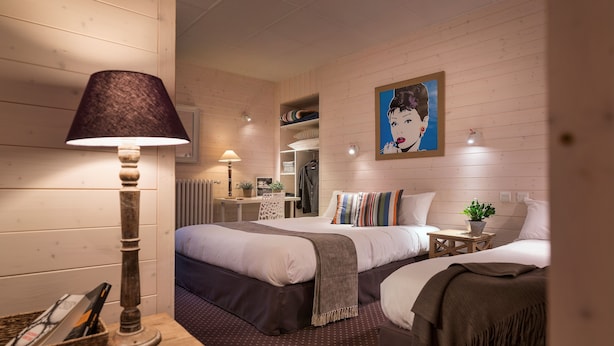 A hotel room with two beds, a desk with a lamp, a mirror, a painting on the wall, and a patterned carpet. - Hôtel des Alpes (Annecy)