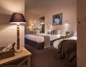 A hotel room with two beds, a desk with a lamp, a mirror, a painting on the wall, and a patterned carpet. - Hôtel des Alpes (Annecy)