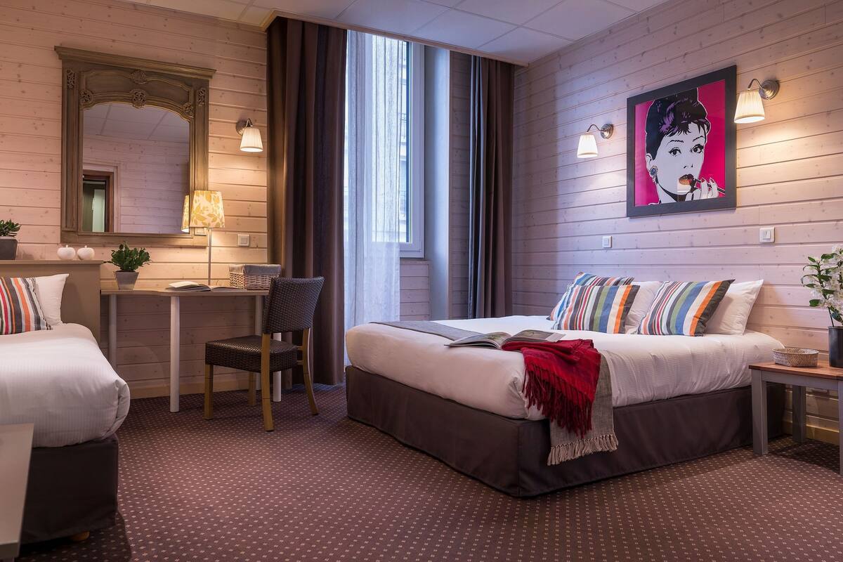 Ett hotellrum med två sängar, ett skrivbord, en stol, en spegel och ett fönster med gardiner.