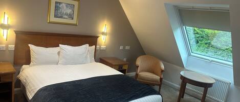 A bedroom with a large bed, two bedside tables, a chair, a small table, a window, and a picture on the wall.