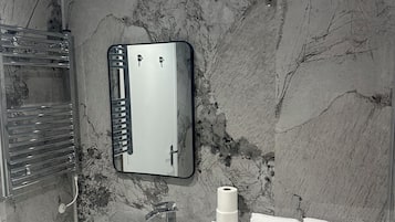 A bathroom with a marble wall, a sink with a mirror, and a towel rack.