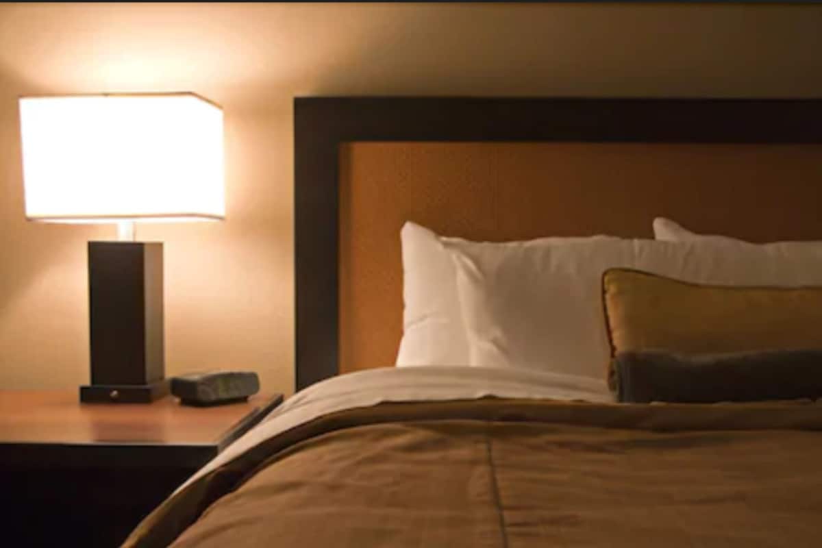 Una habitación de hotel con una cama, una mesita de noche con lámpara y un cabecero de madera.
