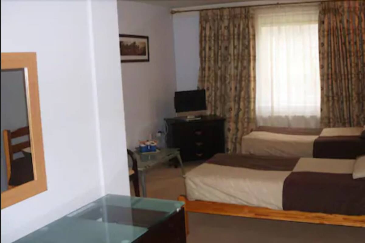 Habitación de hotel con dos camas, un televisor sobre un mueble bajo, un escritorio con una silla y una ventana con cortinas.