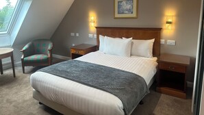 Ein Schlafzimmer mit einem großen Bett, einem Sessel, einem kleinen Tisch und einem Bild an der Wand.