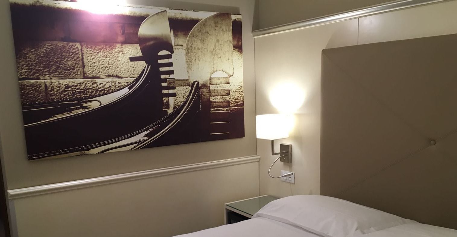 Une chambre d’hôtel avec un lit, une lampe fixée au mur et un grand tableau représentant un pont.