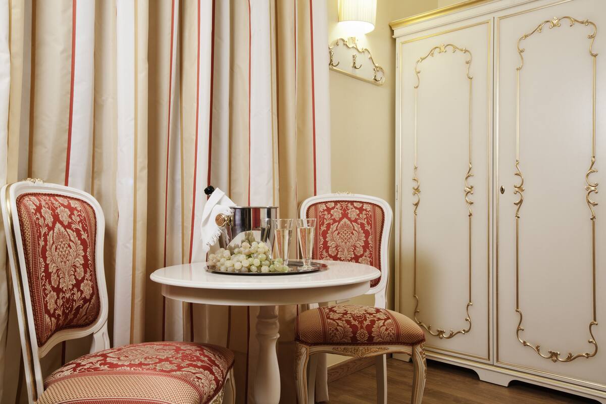 A dining area with two ornate chairs, a table with a glass centerpiece, and a white cabinet with gold trim.