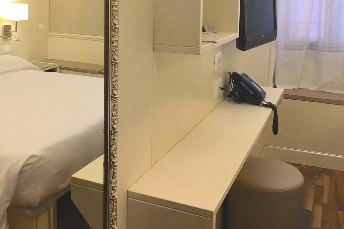 A hotel room with a bed, a desk with a telephone, a television, and a mirror.
