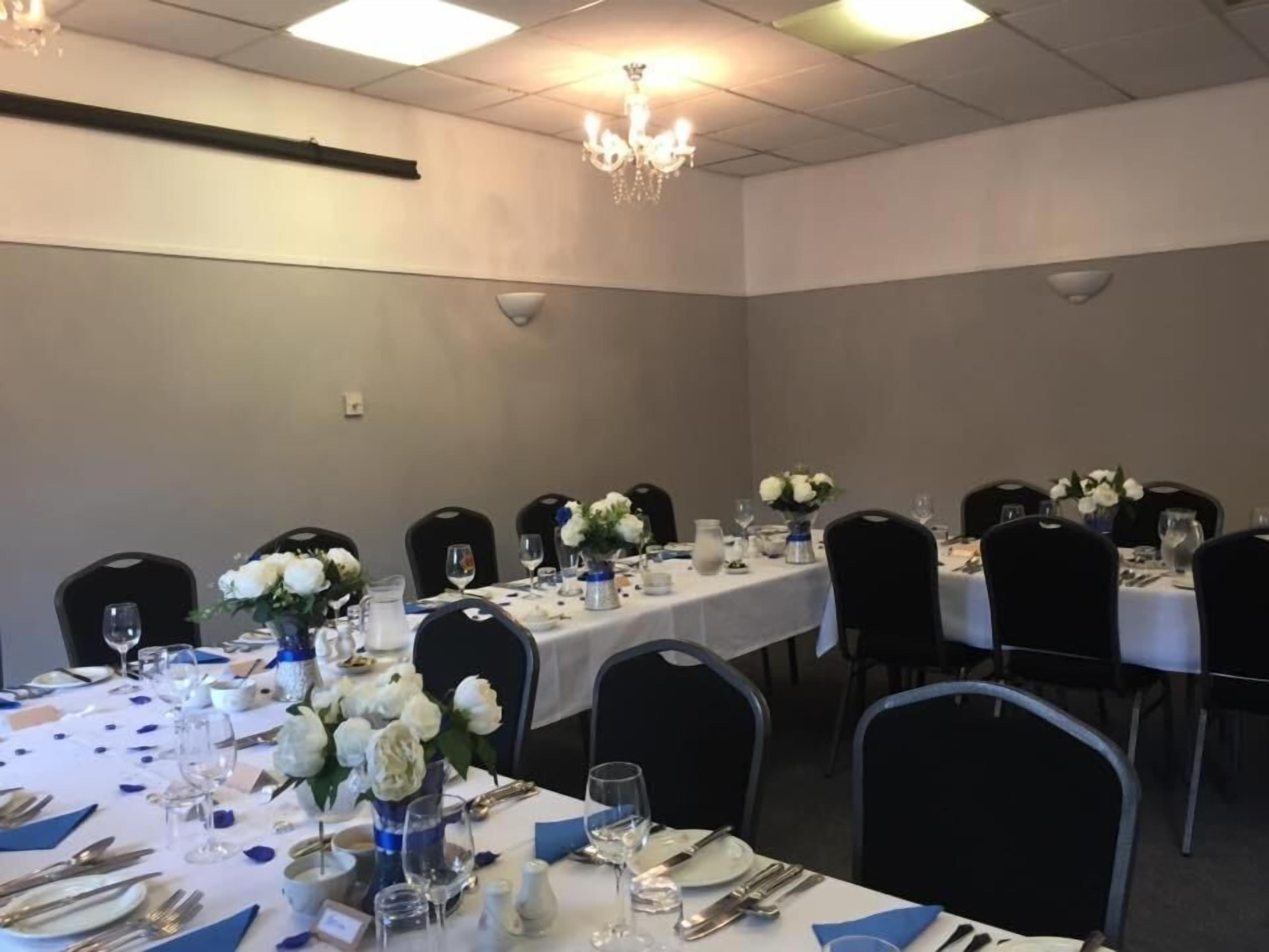 A banquet hall with tables set for a formal event, featuring white tablecloths, floral centerpieces, and black chairs.