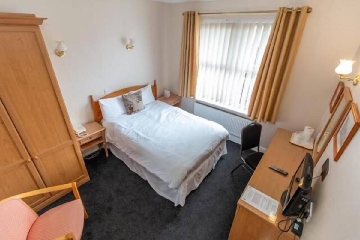Une chambre d’hôtel comprenant un lit, un bureau, une chaise, une armoire et une fenêtre avec des rideaux.