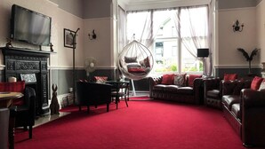 Een ruime woonkamer met een rood tapijt, leren banken, een hangstoel, een open haard en een groot raam met gordijnen.