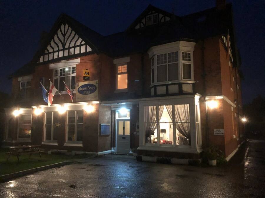 Um hotel de estilo Tudor tradicional, com uma janela saliente e uma placa indicando ser o Quorn Lodge Hotel.
