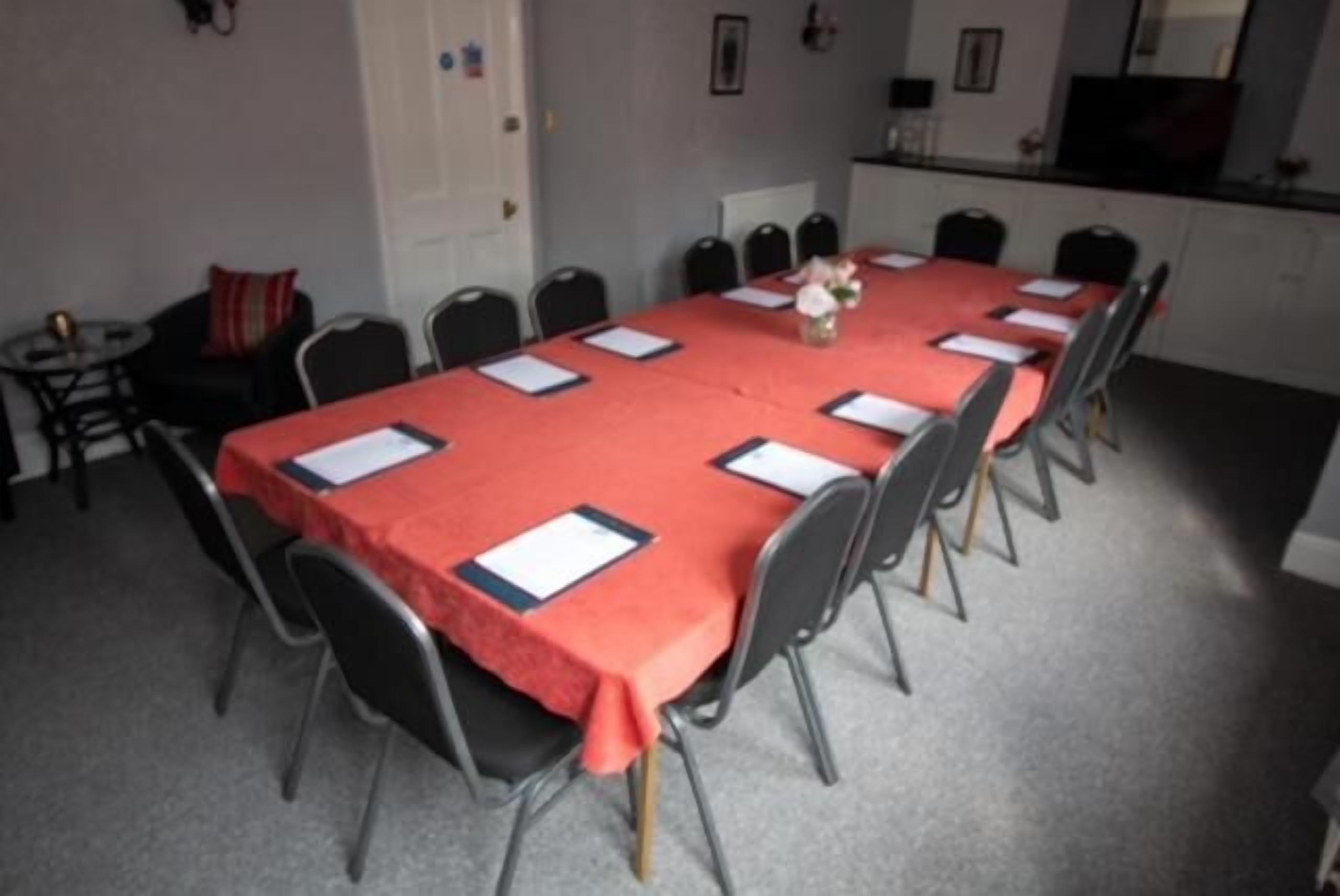 A conference room with a long table covered in a red tablecloth, surrounded by chairs.