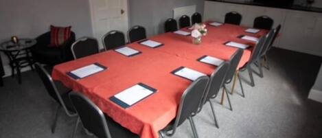 A conference room with a long table covered in a red tablecloth, surrounded by chairs.