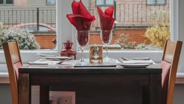 Een eettafel gedekt met twee rode servetten, een glas en een klein decoratief object.