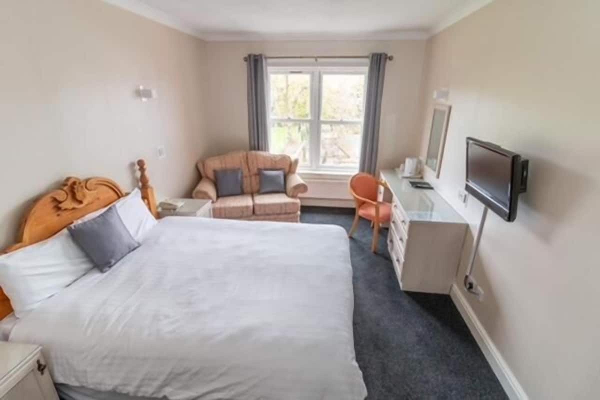 Une chambre d’hôtel avec un grand lit, un bureau avec une chaise, une télévision et une fenêtre avec des rideaux.