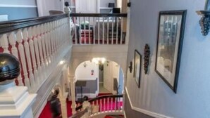 Een meerlaagse trap met roodgekleurde tredes, witte balustrades en uitzicht op een kamer met een bed en nachtkastje.