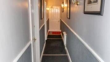A narrow hallway with a carpeted floor, white trim, and framed pictures on the walls.