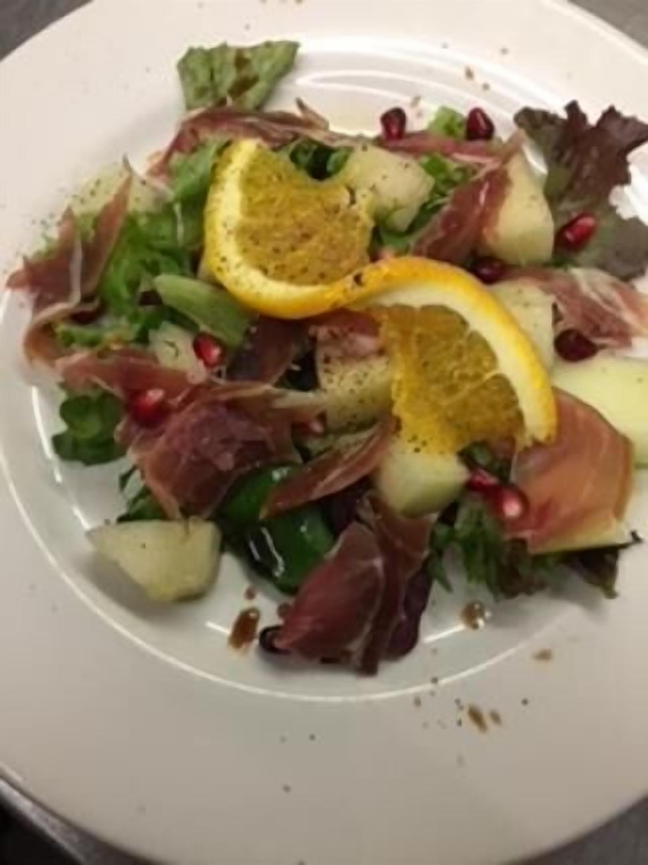 A plate of mixed greens, prosciutto, and pomegranate seeds.