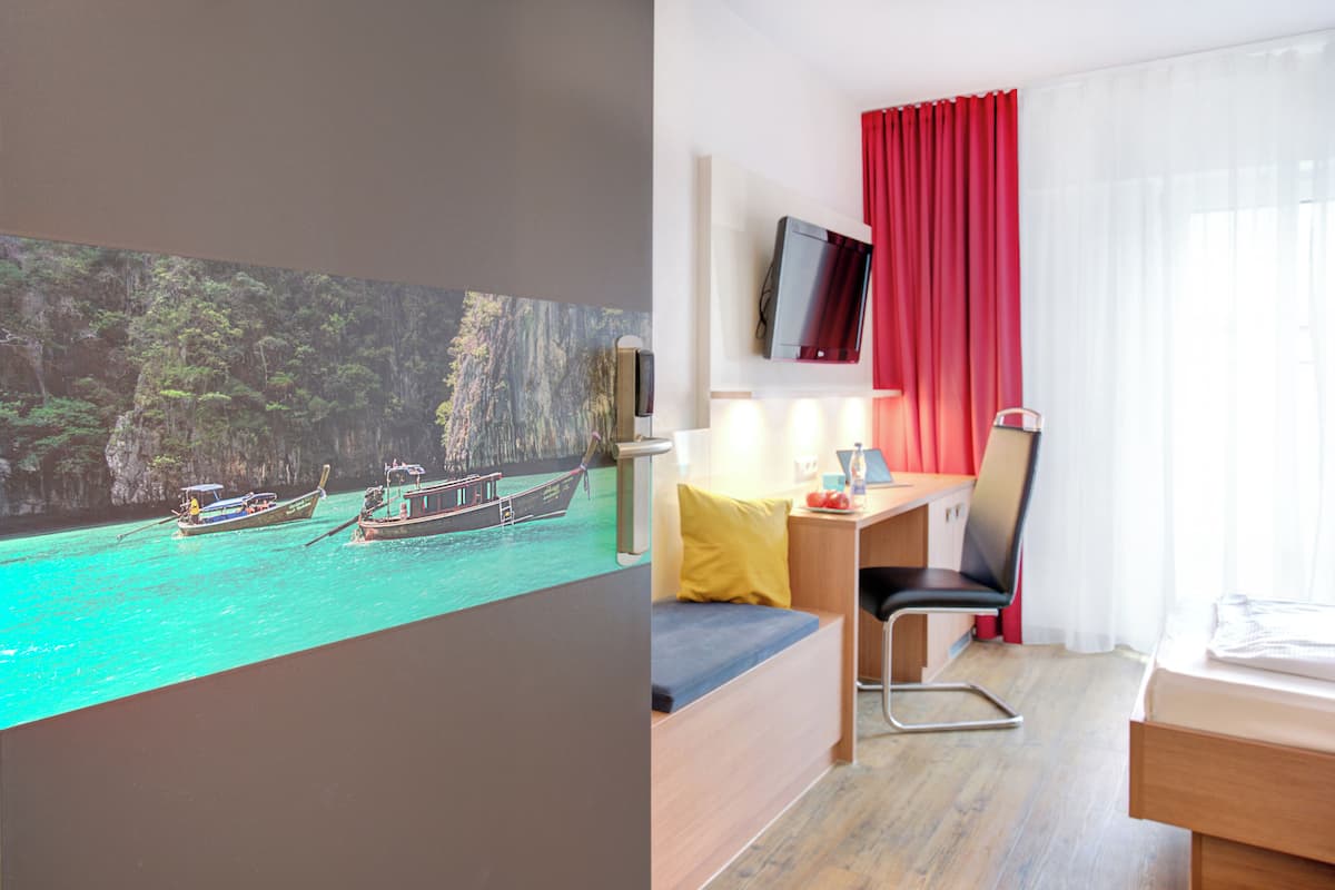 Ein Hotelzimmer mit Bett, Schreibtisch, Stuhl, Fernseher und einem Bild von Booten auf dem Wasser.