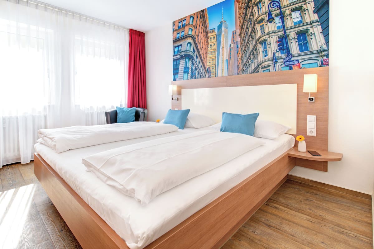 Ein Hotelzimmer mit zwei Betten, einem großen Gemälde von Stadtgebäuden, einem roten Vorhang und einem Holzboden.
