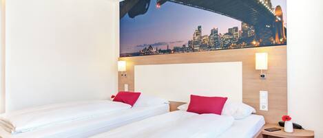 Habitación de hotel con dos camas, un mural de paisaje urbano en la pared y una mesita de noche con un teléfono y un florero.
