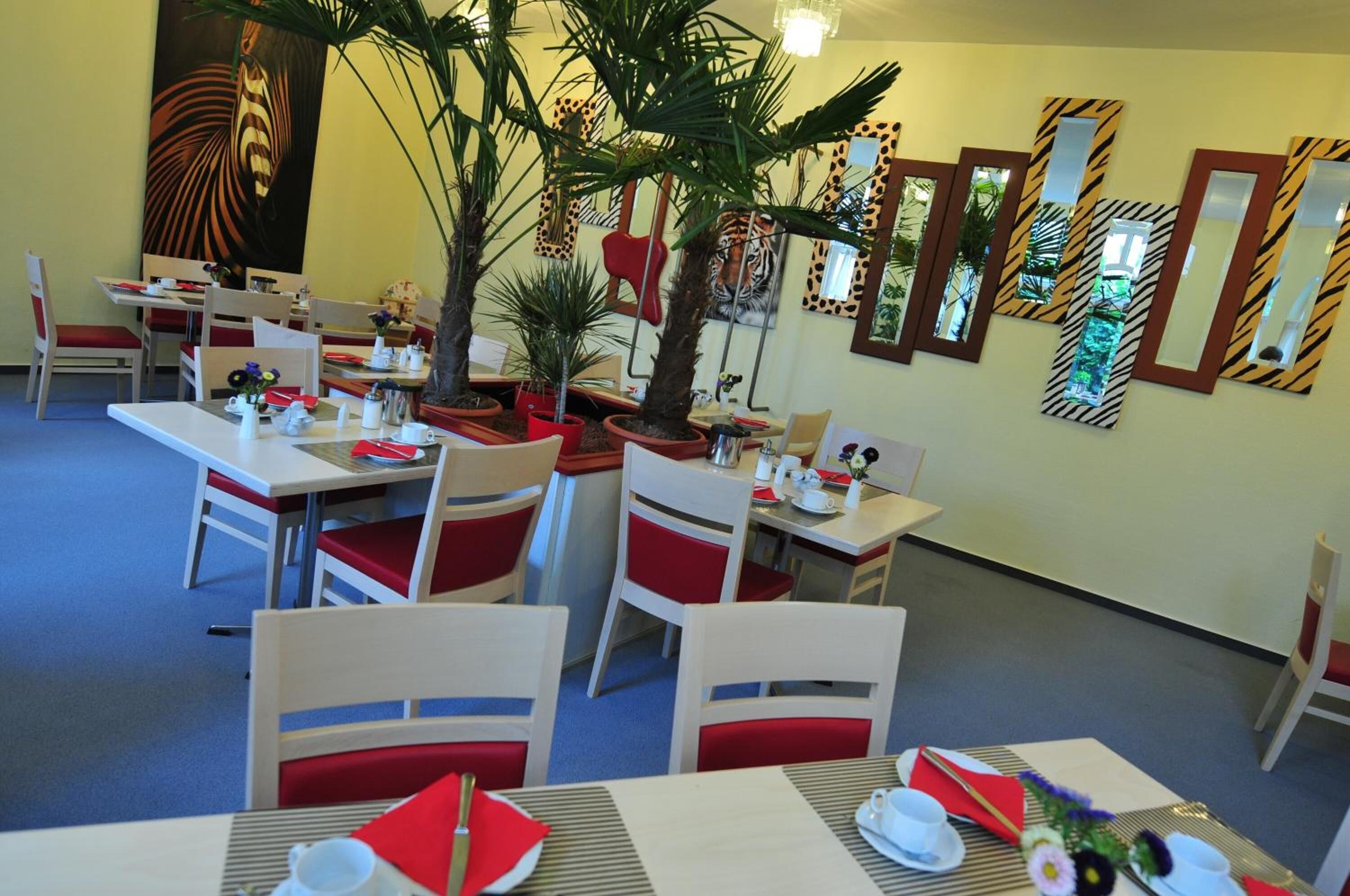 A dining area with tables set for four, each with red and white chairs, and a large painting on the wall.