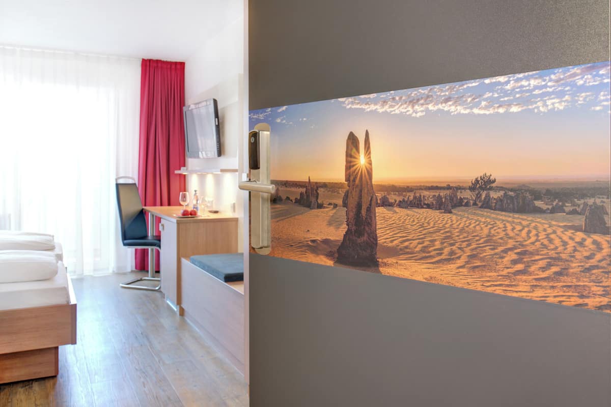 Ein modernes Hotelzimmer mit einem Bett, einem Schreibtisch, einem Sessel und einem Fernseher an der Wand.