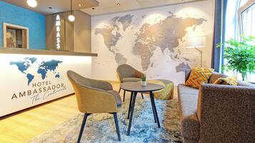 A hotel lobby with a world map wall, comfortable seating, and a reception desk.