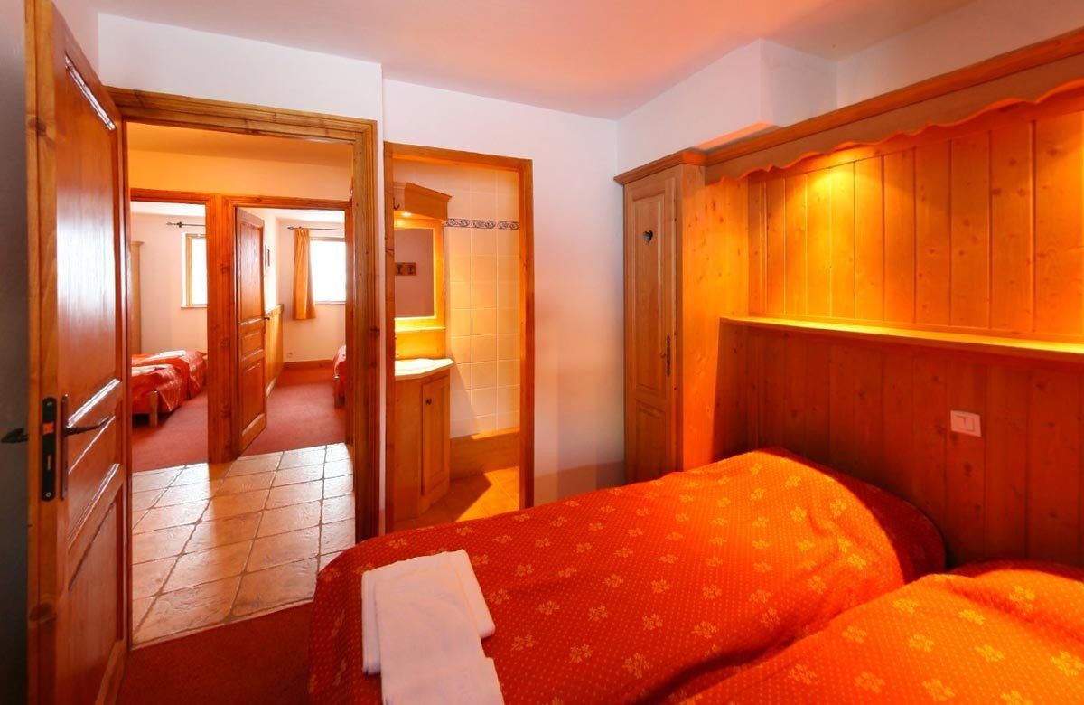 A hotel room with two beds, wooden wardrobe, and a bathroom visible through an open door.