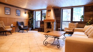 A cozy lounge area with a stone fireplace, comfortable seating, and large windows offering views of the surrounding landscape. - Chalet des Neiges - Oz en Oisans (Oz)