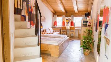 A wooden staircase leading to a loft bedroom with a bed, a desk, and a potted plant.